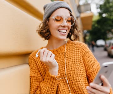 Girl in gray hat in sunglasses and orange sweater listening to music