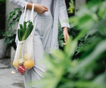 A girl in a striped light suit carries a wicker bag with vegetables